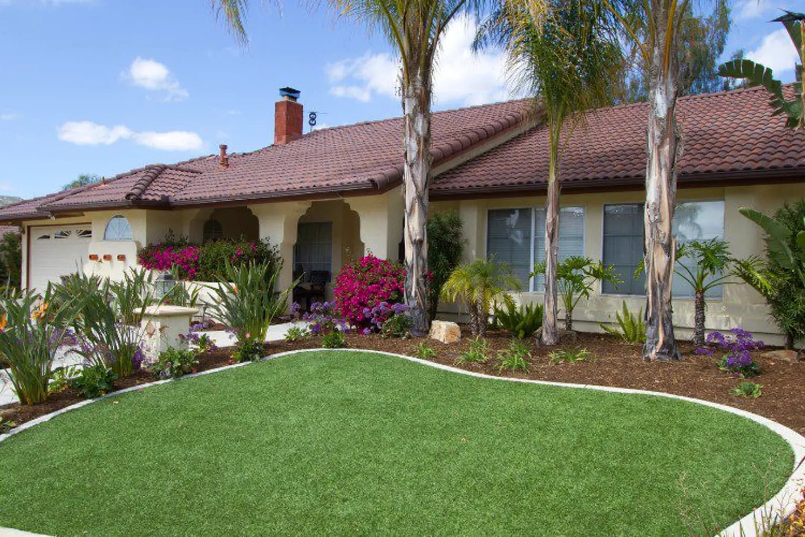 Front-yard artificial turf installation with palm trees and accent plantings in Kern County
