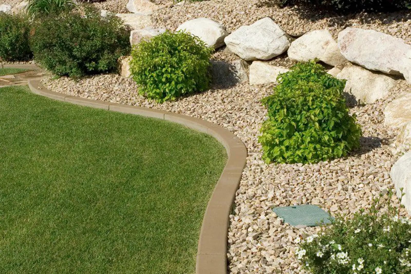 Curved hardscape edging with decorative boulders framing a manicured lawn